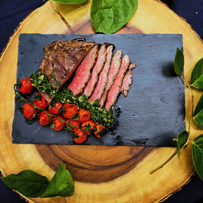 Charred Tomatoes and Flank Steak on a Stone Slate. Greenery and wooden background